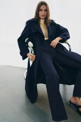 Jeans de tiro alto con corte flare y ajuste slim. Presenta trabillas en la cintura, bolsillos delanteros con detalle de botones metálicos y raya planchada a lo largo de las piernas. Cierre frontal con cremallera y botón.