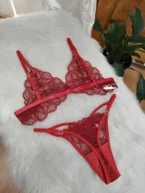 Conjunto de lencería compuesto por un bralette y una tanga, ambos confeccionados en encaje rojo con detalles de tiras elásticas. El bralette presenta un diseño triangular sin aros, mientras que la tanga cuenta con laterales ajustables y diseño de tiras.