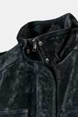 Cazadora de ante con cuello subido, cierre frontal con cremallera y botones a presión ocultos. Presenta bolsillos con solapa en el pecho, bolsillos de vivo en el delantero, trabillas en los hombros y bajo con acabado elástico.