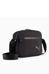 Bandolera Puma modelo 092184, color negro, de diseño rectangular con compartimento principal con cierre, bolsillo frontal con cremallera y correa ajustable para el hombro. Incluye el logo de la marca estampado en plateado.