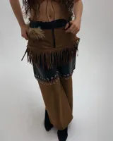 Pantalón largo de diseño audaz que combina cuero sintético negro en la parte superior y gamuza marrón en la inferior, unidas por una hilera de argollas metálicas. Cuenta con detalles de flecos en la cadera y aplicación de piel sintética en la cintura.