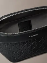 Riñonera Calvin Klein de poliuretano color negro, con diseño de monograma grabado en relieve, cierre superior de cremallera, bolsillo frontal con cremallera y correa ajustable.