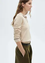 Jersey de punto fino en color beige, con cuello tipo polo y solapa, manga larga con puños acanalados y ribetes en contraste.