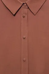 Camisa celeste de manga larga con cuello solapa y pliegues en los puños. Presenta cierre frontal con botones forrados al tono y bajo asimétrico.