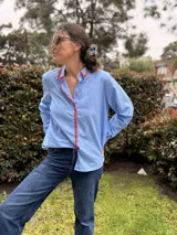 Camisa celeste a rayas con cuello y botonera decorados con bordado artesanal en hilo rojo, de corte clásico y mangas largas.