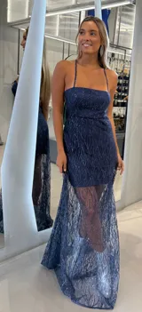 Vestido largo de fiesta color azul marino con diseño de brillos en patrón de hojas. Presenta un corte tipo strapless con breteles finos, una falda corta interior y una sobrecapa de tul transparente con tajo lateral.