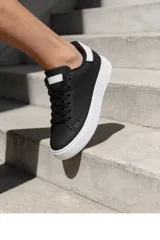 Champion de estilo urbano color negro con suela blanca, confeccionado en material sintético con cordones negros y detalle en blanco en la lengüeta y el talón.
