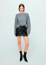 Minifalda de corte recto efecto piel, color negro, con diseño corto y adorno de tachuelas metálicas repartidas por la superficie. Cuenta con cierre de cremallera lateral y forro interior.