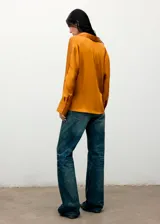 Camisa de tejido satinado en color mostaza, con diseño cruzado, cuello camisero, manga larga con puños abotonados y cierre delantero de botones ocultos.