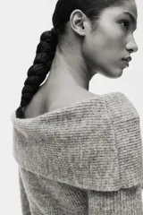 Buzo de punto acanalado con escote off-the-shoulder y detalle de nudo frontal. Presenta mangas largas y diseño ajustado.