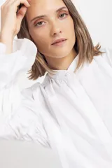 Camisa blanca de algodón con cuello mao, cierre frontal oculto y mangas largas fruncidas con volumen.