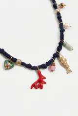 Collar corto de tela azul marino tipo organza, decorado con múltiples charms colgantes que incluyen dijes de peces metálicos, un coral rojo, cuentas de vidrio de colores, perlas y elementos metálicos dorados. Cuenta con cadena de alargue y cierre de mosquetón.