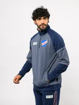 Buzo deportivo de medio cierre marca Umbro del Club Nacional de Football. Presenta un diseño en tonos azul y gris jaspeado, con cuello alto, mangas largas y detalles de costuras en contraste. Incluye el escudo del club y logo de la marca en el pecho.
