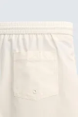 Short de baño de color beige con textura seersucker, cintura elástica con cordón ajustable, bolsillos laterales y forro interior.