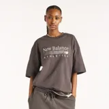 Remera New Balance de algodón gris oscuro con cuello redondo y mangas cortas. Presenta un diseño de corte holgado y estampado gráfico bordado en el pecho con las inscripciones "New Balance Athletics".