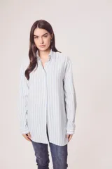 Camisa oversize celeste y blanca a rayas verticales, de mangas largas con puños abotonados y cuello camisero.