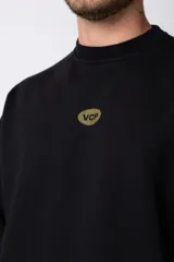 Buzo de cuello redondo y corte oversize, confeccionado en frisa suave. Presenta un diseño minimalista en color negro con un pequeño logo ovalado en el centro del pecho y una estampa sutil en el lateral inferior derecho.