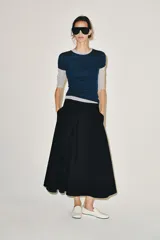 Falda midi color beige confeccionada en hilatura con mezcla de algodón. Presenta tiro medio, cintura con trabillas, bolsillos laterales ocultos en costura y cinturón del mismo tejido. Su diseño incluye un bajo acabado en línea evasé y cierre lateral con cremallera.