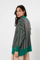 Sweater verde esmeralda de cuello redondo y manga larga, con terminación acanalada en puños y ruedo. Presenta tajos laterales y diseño de rayas verticales en tonos blanco y rosa.