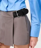 Short pollera sastre de color marrón oscuro, con diseño de plegado delantero que simula una pollera, cintura estructurada y cinturón lateral integrado con hebilla metálica.