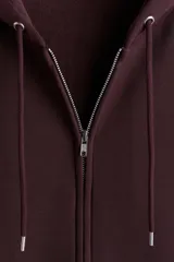 Campera con capucha de felpa color marrón oscuro (vino/borgoña), con interior cepillado suave. Presenta hombros caídos, cierre frontal, cordón para ajustar la capucha y bolsillos canguro delanteros. Puños y bajo terminados en punto acanalado.