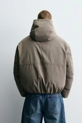 Cazadora de corte relajado confeccionada en tejido técnico con interior acolchado. Presenta cuello subido con capucha, cierre frontal de cremallera, bolsillos de vivo en la cadera y puños y bajo con acabado elástico.