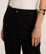 Pantalón zanahoria de poliéster y elastano color negro, de tiro alto, con cierre tradicional, bolsillos traseros y botón metálico con efecto martillado.