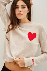 Sweater de punto color beige, con cuello redondo y manga larga. Presenta un corazón rojo bordado en el pecho y la palabra 'l'amour' bordada en el puño de la manga.