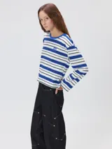 Remera de manga larga con diseño a rayas horizontales en tonos azul, blanco y negro. Presenta un cuello redondo al tono y un logo bordado en el pecho. El diseño destaca por tener un patrón de rayas diferente en las mangas y un calce holgado.