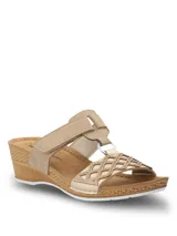 Sandalias de plataforma baja con diseño de tiras cruzadas en color beige y dorado. Presentan una tira superior con cierre de velcro y una tira frontal con detalle de calados geométricos y pequeñas tachas metálicas. La plantilla es acolchada y la suela tiene textura tipo yute.