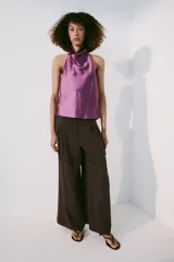 Top halter confeccionado en tejido satinado de color lila, con escote fluido y hombros descubiertos. Presenta cierre en la espalda con botón oculto.