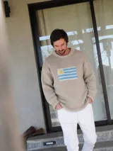 Sweater de tejido de punto color beige con diseño de la bandera de Uruguay en el centro del pecho, cuello redondo y mangas largas.