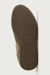 Zapatilla deportiva de estilo casual, confeccionada en una combinación de piezas de cuero con acabado serraje. Presenta horma redonda, cierre con cordones y suela dentada en contraste.