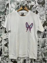Remera blanca de algodón con estampado de una mariposa azul y violeta en el lado izquierdo del pecho.