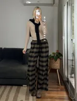 Pantalón tipo palazo de corte amplio y tiro alto, confeccionado en tela con estampado de cuadros escoceses en tonos marrones, blancos y negros. Cuenta con cintura elástica y bolsillos laterales.