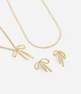 Conjunto de joyería bañado en tono dorado claro (light gold), compuesto por un par de caravanas (aretes) y dos collares. Un collar tiene cadena lisa tipo serpiente y el otro presenta un colgante con forma de lazo estilizado. Las caravanas también tienen forma de lazo.