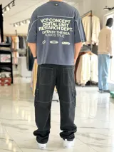 Remera gris oscuro con corte boxy fit de manga corta y cuello redondo. Cuenta con un diseño gráfico frontal con la palabra "CONCEPT" en grandes letras blancas delineadas y líneas decorativas horizontales y en las sisas.