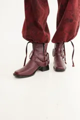 Bota de caña baja confeccionada en cuero con textura crocco, color bordó. Presenta taco cuadrado, punta cuadrada y un accesorio desmontable con doble hebilla metálica y tachas decorativas.