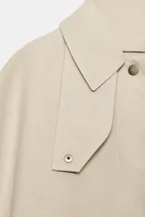 Trench de cuello con solapa y manga larga, con detalle de capa desmontable del mismo tejido en la parte superior. Cuenta con cierre frontal de botones y bolsillos en el delantero.