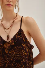 Top de tirantes finos con escote en V y detalle de volados en el borde. Presenta un estampado abstracto en tonos marrones y ocres, con un diseño fluido y ligero.
