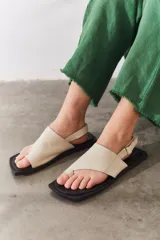 Sandalias de cuero color marrón con diseño de dedo, tira ajustable en el talón y suela plana de color negro.