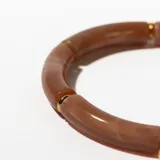 Pulsera rígida de color rosa con vetas blancas, compuesta por segmentos tubulares unidos por anillos dorados. Incluye un dije dorado en forma de gota.