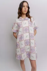 Vestido corto beige con estampado botánico en negro, cuello camisero, mangas cortas y cierre frontal con botones.