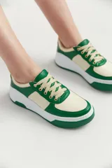 Zapatillas urbanas color crema con detalles en verde, cordones color crema y suela blanca.