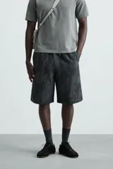 Bermuda de corte relajado, color gris oscuro con efecto tie-dye o textura irregular. Presenta cintura elástica ajustable con cordón y bolsillos laterales y traseros de plastrón.