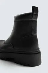 Bota de caña media con cierre frontal mediante cremallera, confeccionada en material con textura. Presenta una horma redonda y una suela de plataforma con diseño track.