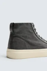 Zapatilla tipo botín de caña alta confeccionada en tejido de algodón color gris oscuro, con suela de goma a contraste en tono crema y cierre de cordones.