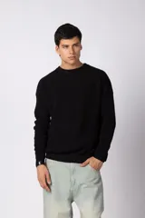 Sweater de tejido de punto acanalado en color negro, con cuello redondo y mangas largas. Presenta un diseño de calce relajado y un pequeño detalle de etiqueta en el puño.
