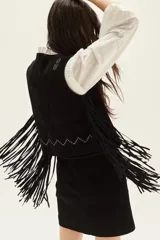 Chaleco de cuero negro con flecos largos en el ruedo y bordados decorativos en hilo claro. Presenta un diseño sin mangas y cierre frontal con lazos.