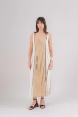 Vestido largo de lino con diseño bicolor en beige y crudo, escote en V y breteles regulables. Presenta detalles de bordados geométricos en el frente y tajos laterales.